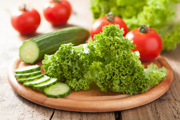 Obraz na płótnie Canvas fresh cucumber tomatoes and salad leaves on chopping board