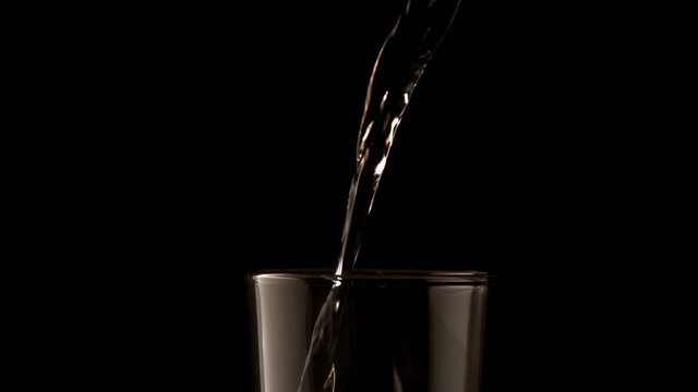 Water pouring into glass on black background