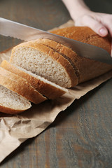 Female hands cutting bread on wooden board, close-up