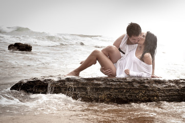 Young beautiful couple kissing on beach rocks