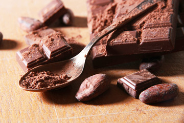 Cocoa powder and dark chocolate on color wooden background