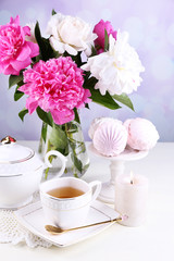 Composition of beautiful peonies in vase, tea in cup and