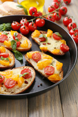 Tasty bruschetta with tomatoes on pan, on old wooden table