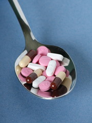 Various pills, tablets and capsules on a silver spoon