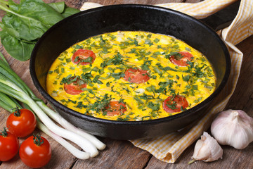 Hot omelette with herbs, tomatoes in a pan and vegetables