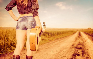 woman in shorts with old guitar on road to horizon