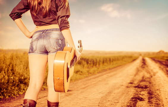 Woman In Shorts With Old Guitar On Road To Horizon