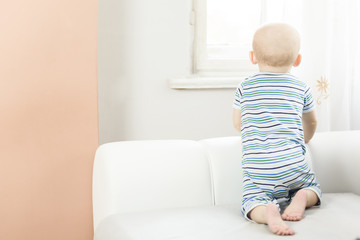 little baby kneeling on the sofa and looks out the window