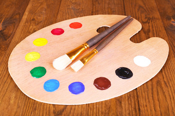 Wooden art palette with paint and brushes on table close-up