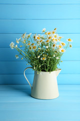Chamomiles in jug  on color wooden background