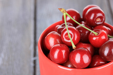 Sweet cherries in mug on wooden background