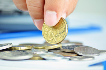 Fingers picking up a coin - one Australian dollar (AUD)