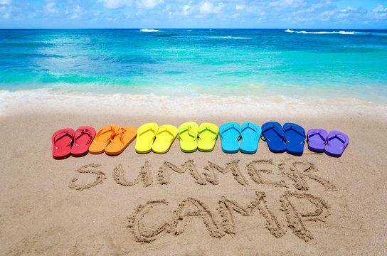 Sign "Summer camp" and color flip flops on sandy beach