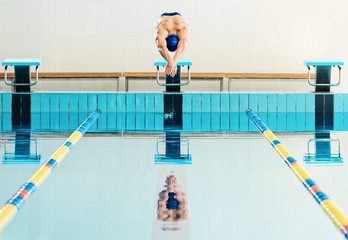 Young muscular swimmer on starting block in a swimming pool