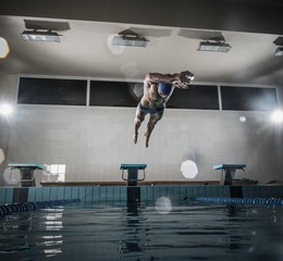 Young muscular swimmer jumping from starting block 