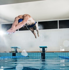 Young muscular swimmer jumping from starting block 
