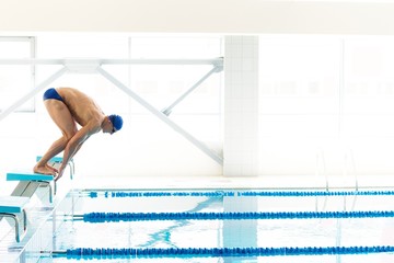 Young muscular swimmer in low position on starting block