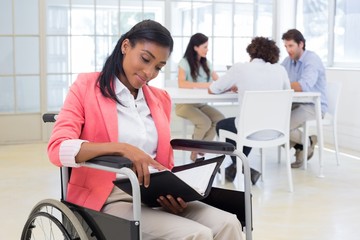 Woman in wheelchair reading document with colleauges in backgrou