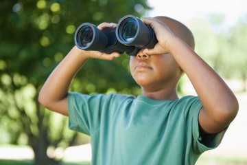 Little boy looking up through binoculars in the park