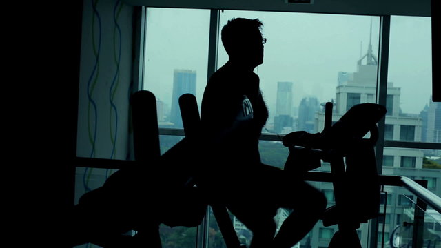Silhouette of man riding stationary bike in the gym
