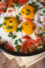 Fried eggs with tomatoes in a pan on the table vertical  macro