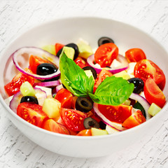 Light greek salad with fresh vegetables, garnished with basil.