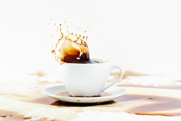 Cup of coffee creating splash. White background, coffee stains.