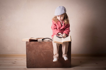 little child with book on suitcase indoor