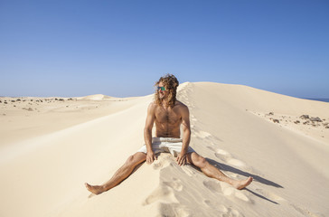 Fototapeta na wymiar young man seated on a desert 's dune