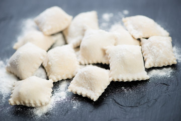 Close-up of raw italian cheese ravioli, black wooden surface