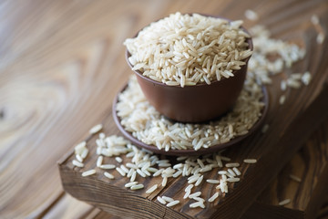 Raw brown rice in ceramic tableware over wooden background