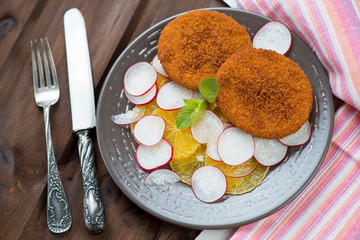 Fried salmon cutlets with orange and radish slices, above view