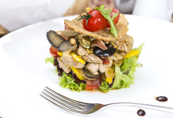 warm salad of vegetables and meat on a plate in a restaurant