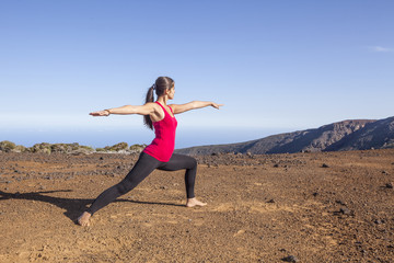 Young woman practicing yoga warrior pose on a desert mountain