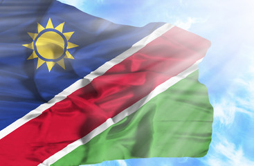 Namibia waving flag against blue sky with sunrays