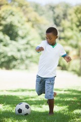 Little boy kicking a football in the park