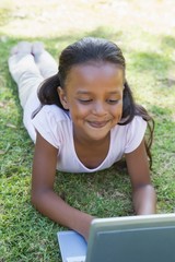 Little girl lying on grass using laptop