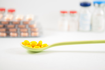 Yellow coating tablet in spoon on vial background
