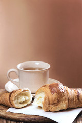 Fresh croissant and cup of tea, on kitchen table.