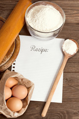 Recipe paper and baking cake ingredients, on a wooden table.