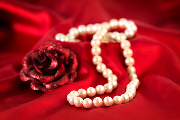 Pearl necklace and red rose on red silk.
