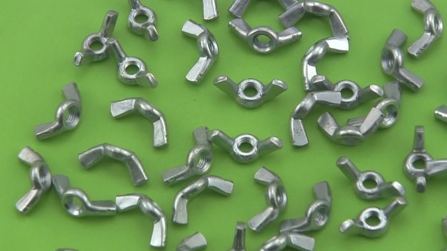 Chrome wing nuts rotating on a green  background.