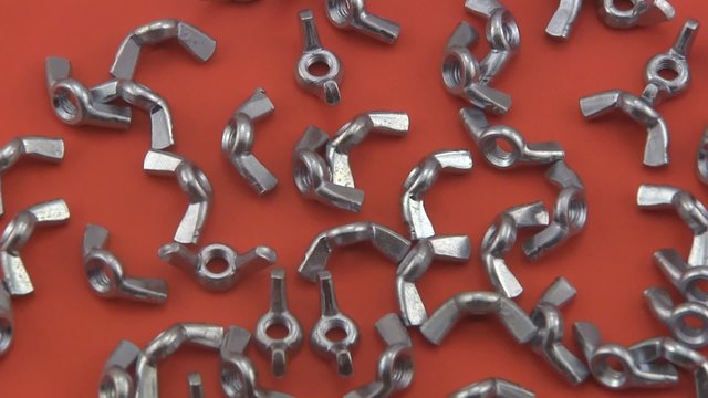Chrome wing nuts rotating on a red  background.
