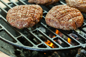 Raw burgers on barbecue grill with fire