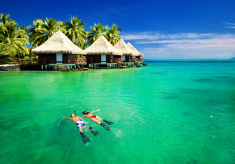 Couple snorkling in lagoon with over water bungalows