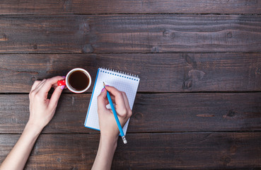 Hands holding notebook and coffee cup.