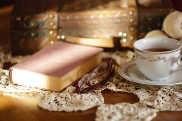 Cup of tea, book and glasses on old wooden table.