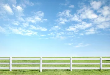 Rolgordijnen white fence on green grass with blue sky © anankkml