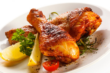Grilled chicken legs and vegetables on white background