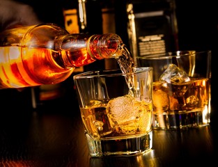 Barkeeper schenkt Whisky vor Whiskyglas und Flaschen ein